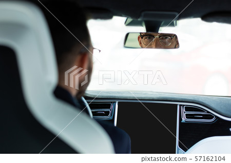 Handsome man wearing glasses looking into rear view mirror 57162104