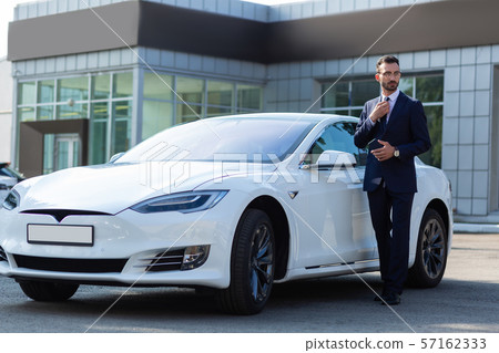 Bearded businessman in dark suit standing near white car Bearded businessman in dark suit standing near white car 57162333