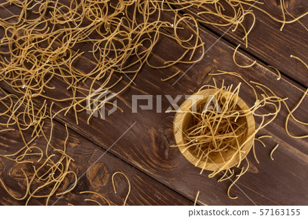 Raw thin noodles on brown wood 57163155