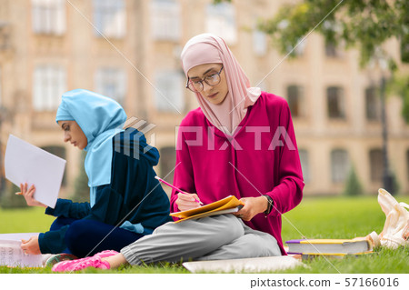 Muslim student wearing glasses studying hard near friend 57166016