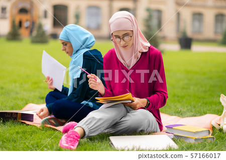 Two muslim students sitting on grass and repeating material 57166017