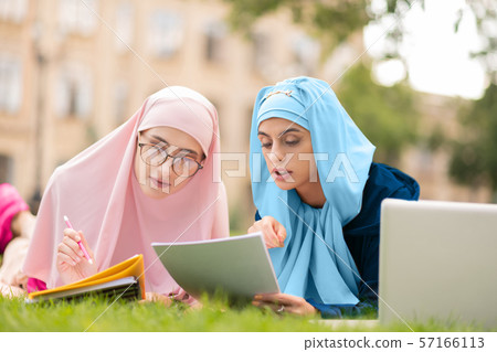 Two muslim students in hijab chilling on lane and reading 57166113