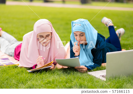 Two muslim students sitting on grass and preparing to exam Two muslim students sitting on grass and preparing to exam 57166115
