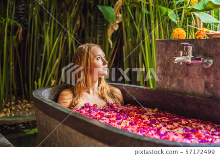 Attractive Young woman in bath with petals of tropical flowers and aroma oils. Spa treatments for 57172499
