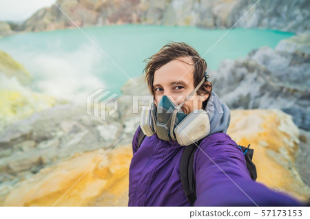 Young man tourist makes a selfie standing at the edge of the crater of the Ijen volcano or Kawah 57173153