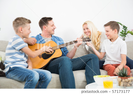 Happy caucasian family smiling, playing guitar and singing songs together at cosy modern home Happy caucasian family smiling, playing guitar and singing songs together at cosy modern home 57173177