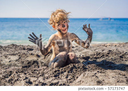 Black Friday concept. Smiling boy with dirty Black face sitting and playing on black sand sea beach 57173747