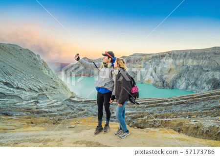 Young tourist man and woman stand at the edge of the crater of the Ijen volcano or Kawah Ijen on the 57173786