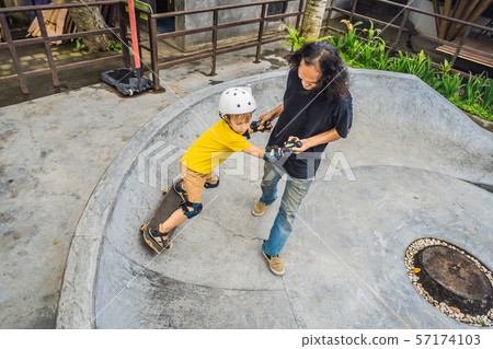 Athletic boy learns to skateboard with asian trainer in a skate park. Children education, sports Athletic boy learns to skateboard with asian trainer in a skate park. Children education, sports 57174103