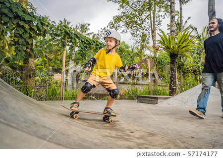 Athletic boy learns to skateboard with a trainer in a skate park. Children education, sports Athletic boy learns to skateboard with a trainer in a skate park. Children education, sports 57174177