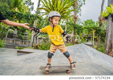 Athletic boy learns to skateboard with a trainer in a skate park. Children education, sports Athletic boy learns to skateboard with a trainer in a skate park. Children education, sports 57174194