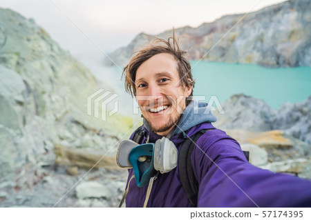 Young man tourist makes a selfie standing at the edge of the crater of the Ijen volcano or Kawah Young man tourist makes a selfie standing at the edge of the crater of the Ijen volcano or Kawah 57174395