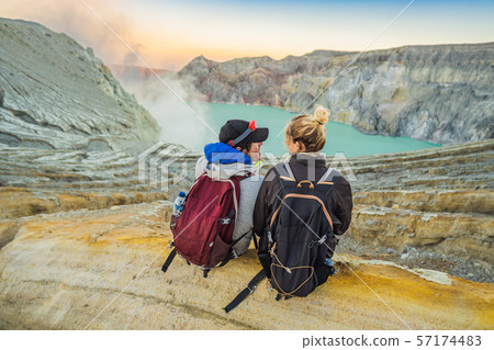 Young tourist man and woman sit at the edge of the crater of the Ijen volcano or Kawah Ijen on the Young tourist man and woman sit at the edge of the crater of the Ijen volcano or Kawah Ijen on the 57174483