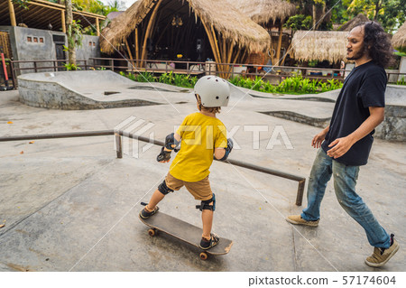 Athletic boy learns to skateboard with a trainer in a skate park. Children education, sports 57174604