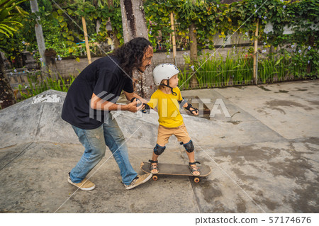 Athletic boy learns to skateboard with a trainer in a skate park. Children education, sports 57174676