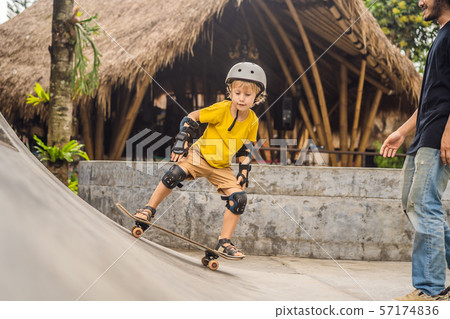 Athletic boy learns to skateboard with a trainer in a skate park. Children education, sports 57174836