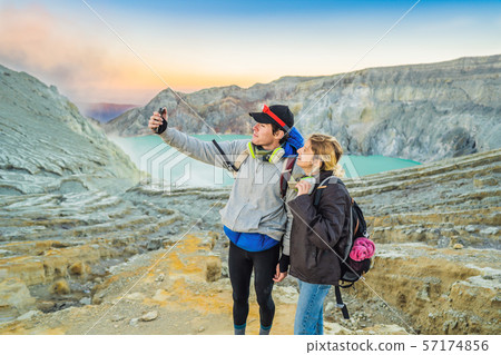 Young tourist man and woman stand at the edge of the crater of the Ijen volcano or Kawah Ijen on the 57174856