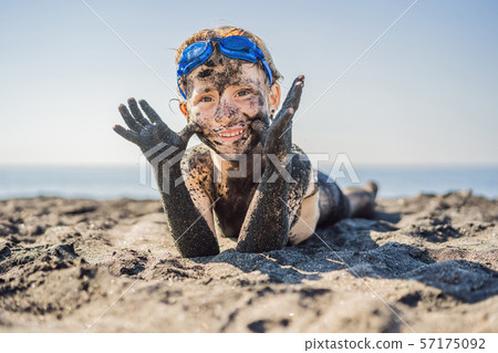 Black Friday concept. Smiling boy with dirty Black face sitting and playing on black sand sea beach 57175092