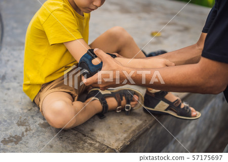 Trainer helps the boy to wear knee pads and armbands before training skate board 57175697