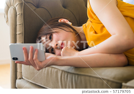 A young lady who lies on the sofa and manipulates the smartphone 57179705