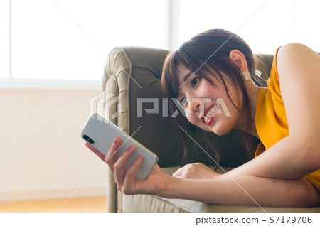 A young lady who lies on the sofa and manipulates the smartphone 57179706