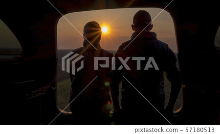 A man and a woman admire the beautiful sunset from the trunk of a car 57180513