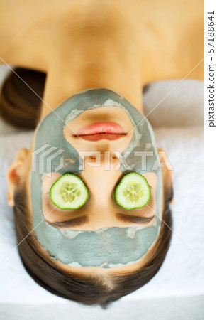 Woman with facial mask and cucumber slices in her hands 57188641