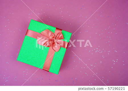 Green gift box with a red bow on a burgundy background with sparkles. Green gift box with a red bow on a burgundy background with sparkles. 57190221