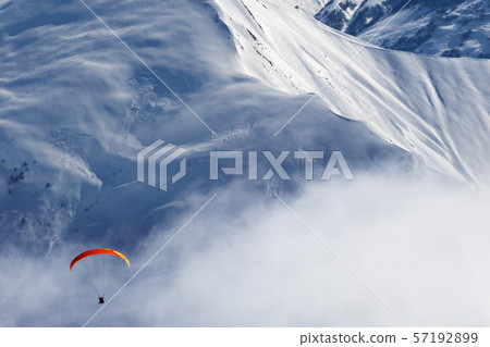 Paragliding at snowy mountains in haze Paragliding at snowy mountains in haze 57192899
