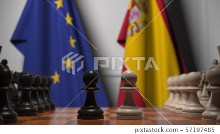 Flags of the EU and Spain behind chess board. The first pawn moves in the beginning of the game Flags of the EU and Spain behind chess board. The first pawn moves in the beginning of the game 57197485