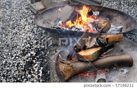 Burning wood of campfire in metal fire bowl on a pebble floor Burning wood of campfire in metal fire bowl on a pebble floor 57198211