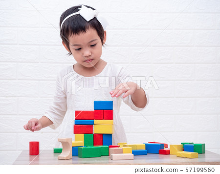 Little cute girl 3-4 years old playing wooden blocks on table and white bricks wall  background. Learning and education. 57199560