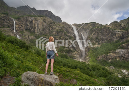 Woman standing on the rock and enjoying the view of epic waterfall Woman standing on the rock and enjoying the view of epic waterfall 57201161