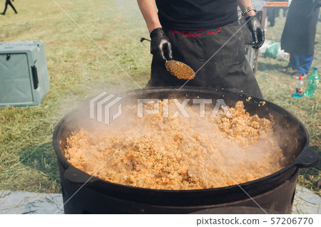 Men putting pilaf from cauldron into container. Men putting pilaf from cauldron into container. 57206770