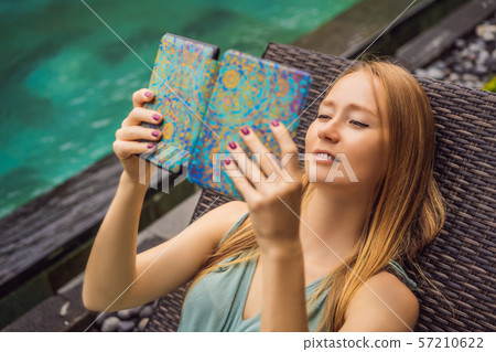 Woman reads e-book on deck chair in the garden 57210622