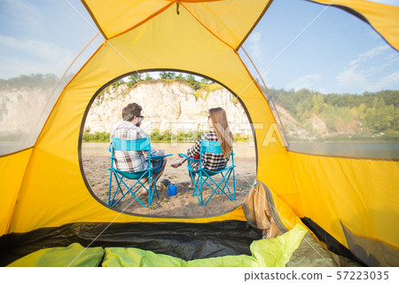 People, tourism and nature concept - Cute couple sitting near yellow tent 57223035