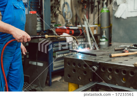 Metalworker heating up piece of metal with burner Metalworker heating up piece of metal with burner 57233561