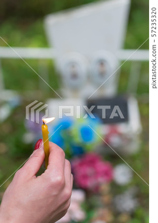 The flame of a wax candle in the hand of a people in the cemetery 57235320
