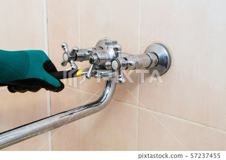 A gloved hand with a wrench repairs the faucet in 57237455