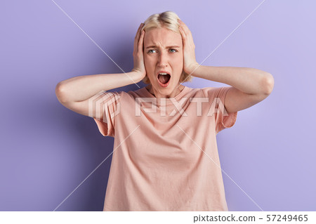 girl closing ears with hands, shouting, looking at camera over violet background. 57249465