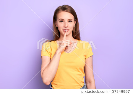 Pretty young lady shows hush gesture with index finger, gossips with friends 57249997