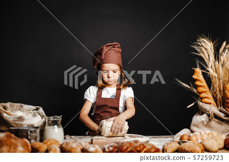 Little girl kneading dough at table 57259723