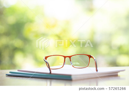 Orange eyeglasses with three white notebook on wooden table, Bokeh garden background, Close up & Macro shot, Selective focus, Stationery concept 57265266
