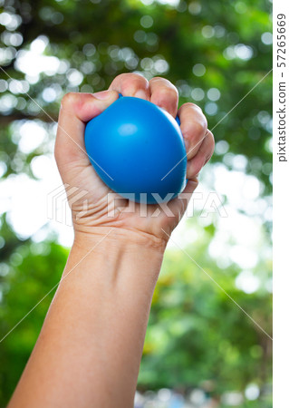 Woman's left hand squeezing blue stress ball on bokeh green garden background, Exercise and Massage concept 57265669