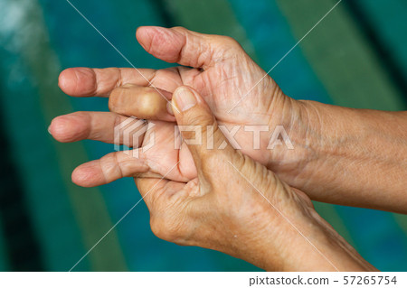Trigger Finger, Senior woman's left hand massaging her middle finger, Suffering from pain, Close up and macro shot, Swimming pool background, Health care concept 57265754