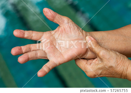 Trigger Finger, Senior woman's left hand massaging her right hand Suffering from pain, Close up and macro shot, Swimming pool background, Health care and massage asian body concept 57265755