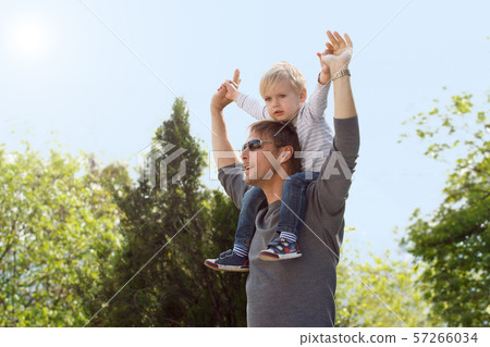 Blond boy sitting on fathers shoulder outdoors 57266034