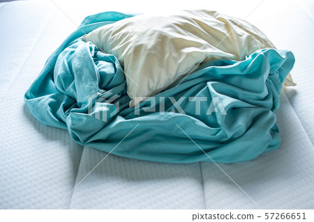 Turquoise crumpled bed sheet with ivory pillow on white bed, Close up shot, Selective focus, Bedroom cleaning concept 57266651
