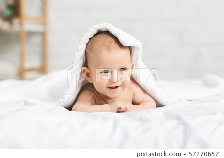 Adorable smiling baby lying on bed under white blanket 57270657