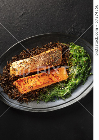 Salmon with sesame seeds, wakame and wild black rice, shot from the top on a black background with a 57274556
